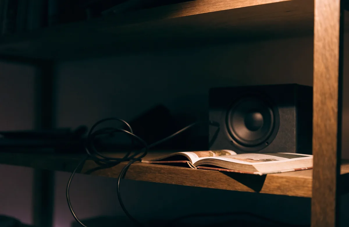 A small speaker and its coiled cable on a shelf, beside a book left open and face down.